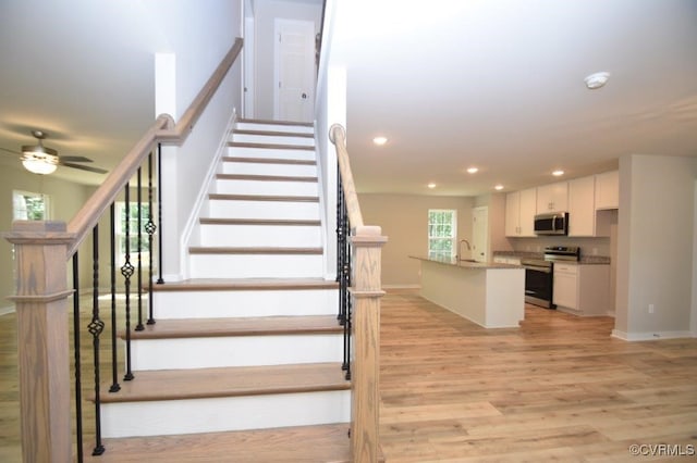 stairs featuring wood-type flooring, sink, and ceiling fan