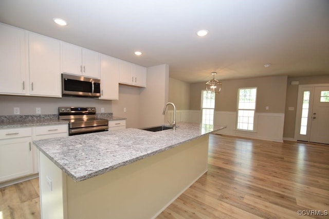 kitchen featuring sink, a kitchen island with sink, white cabinetry, stainless steel appliances, and light stone countertops