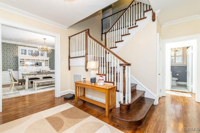 stairway with crown molding, hardwood / wood-style floors, and an inviting chandelier