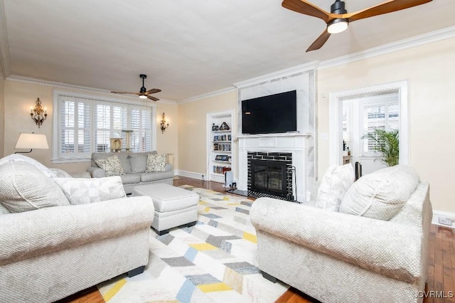 living room with a tiled fireplace, ornamental molding, ceiling fan, and light hardwood / wood-style floors