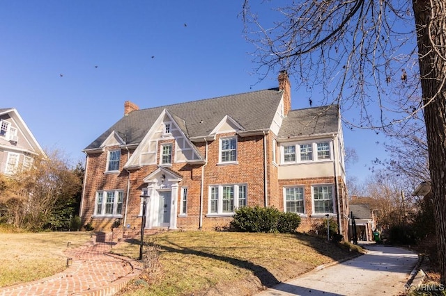 view of front of home featuring brick siding, a chimney, and a front lawn