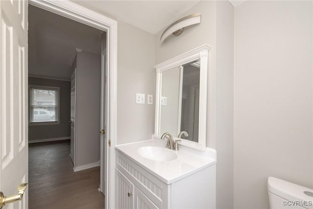 half bath featuring baseboards, vanity, toilet, and wood finished floors