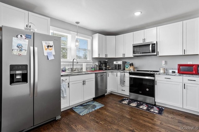 kitchen with stainless steel appliances, a sink, white cabinets, hanging light fixtures, and dark wood-style floors