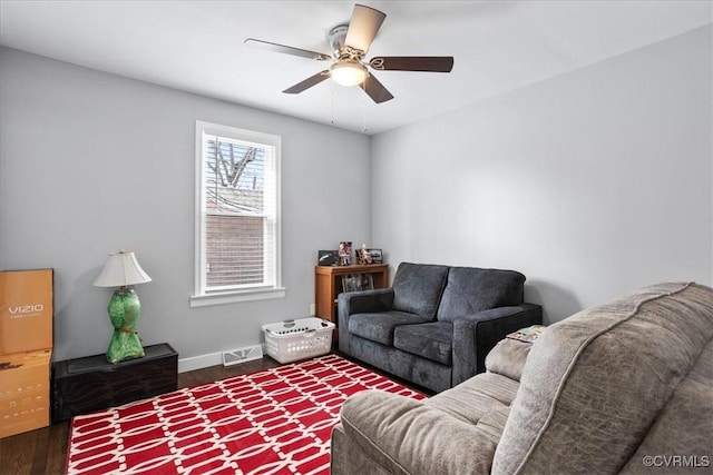 living area featuring a ceiling fan, visible vents, baseboards, and wood finished floors