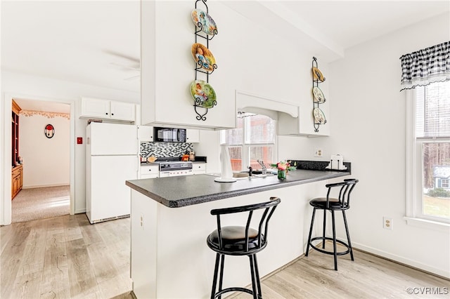 kitchen with a peninsula, dark countertops, freestanding refrigerator, and white cabinetry