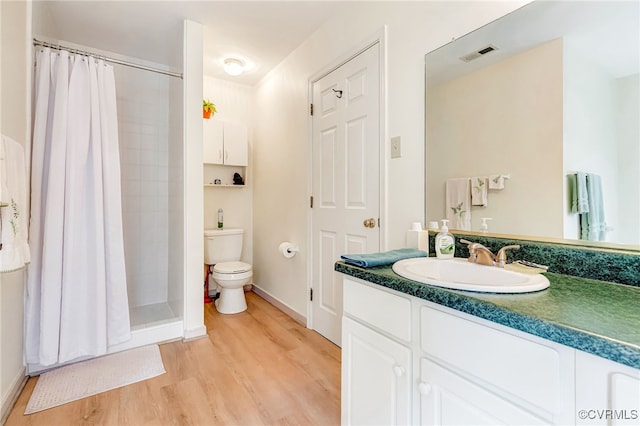 bathroom with a stall shower, visible vents, toilet, wood finished floors, and vanity