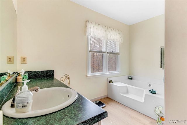 full bathroom featuring baseboards, vanity, a bath, and wood finished floors