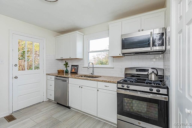 kitchen with appliances with stainless steel finishes, sink, white cabinets, and dark stone counters