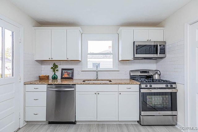 kitchen featuring white cabinetry, stainless steel appliances, light stone countertops, and sink