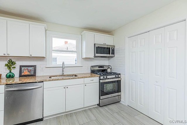 kitchen featuring appliances with stainless steel finishes, sink, white cabinets, decorative backsplash, and light stone countertops