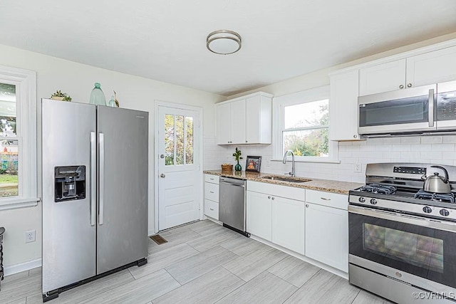 kitchen with appliances with stainless steel finishes, sink, white cabinets, decorative backsplash, and light stone countertops