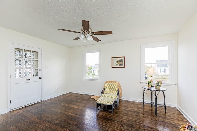 living area with ceiling fan, dark wood-type flooring, and a textured ceiling