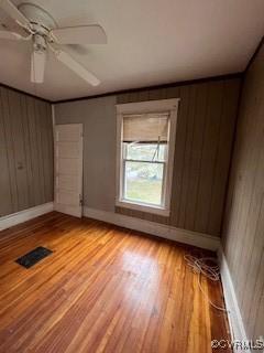 empty room featuring wooden walls, baseboards, visible vents, ceiling fan, and light wood-type flooring