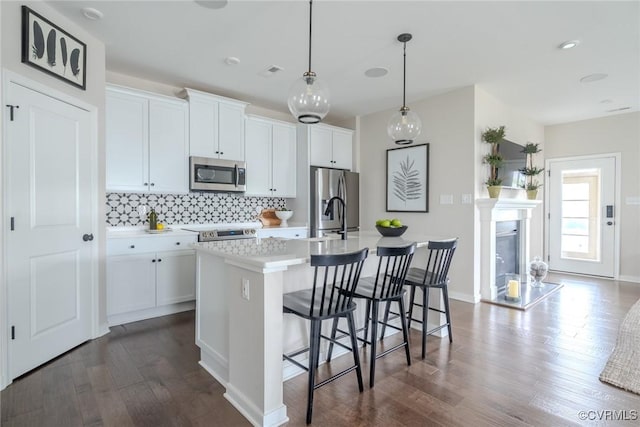 kitchen with stainless steel appliances, an island with sink, white cabinetry, and decorative light fixtures