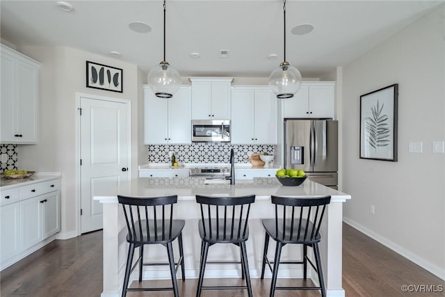 kitchen with appliances with stainless steel finishes, decorative light fixtures, an island with sink, and white cabinets