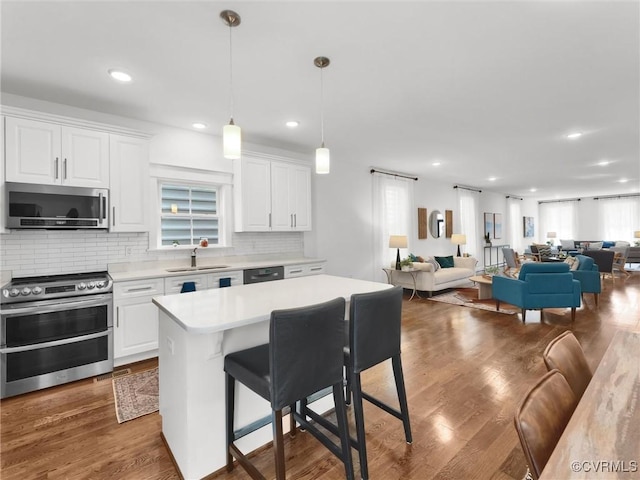 kitchen with appliances with stainless steel finishes, pendant lighting, white cabinetry, a breakfast bar area, and a center island