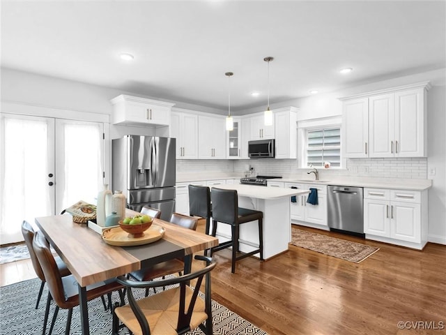 kitchen with white cabinetry, dark hardwood / wood-style flooring, a kitchen island, pendant lighting, and stainless steel appliances