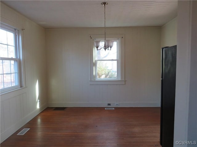 unfurnished dining area with dark wood-type flooring and an inviting chandelier