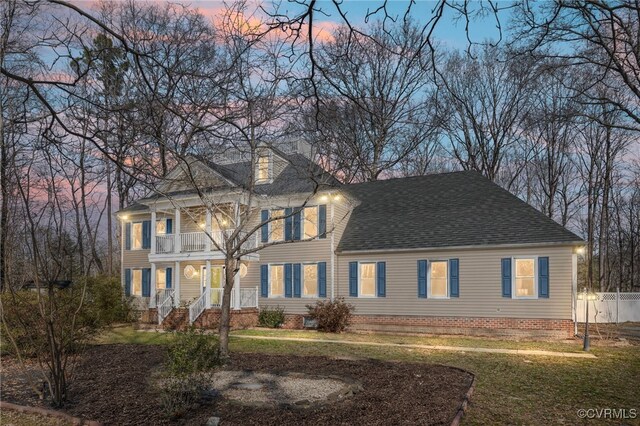 view of front facade featuring a balcony, a chimney, a lawn, and roof with shingles