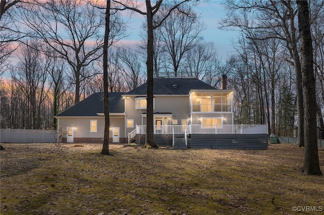 back of property at dusk with a yard, fence, and a sunroom