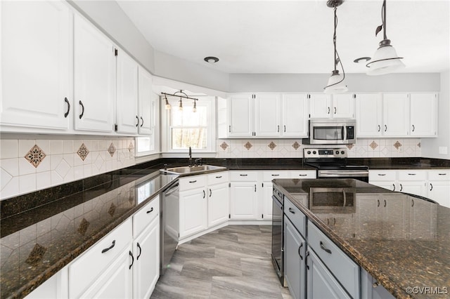 kitchen with stainless steel appliances, a sink, white cabinets, hanging light fixtures, and dark stone countertops