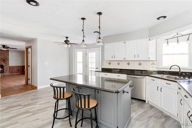 kitchen featuring white cabinets, a center island, hanging light fixtures, stainless steel dishwasher, and a sink