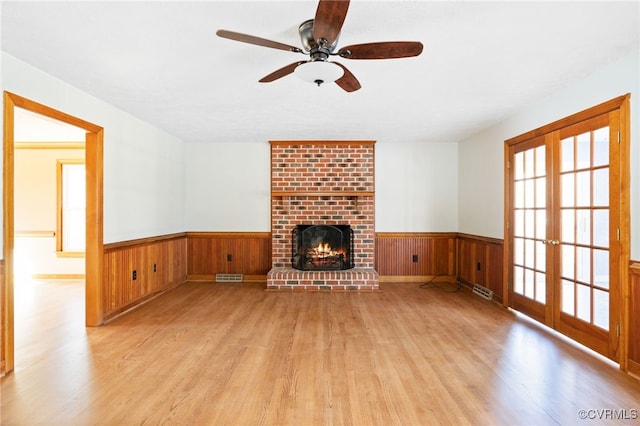 unfurnished living room featuring wooden walls, visible vents, wainscoting, light wood-type flooring, and a brick fireplace