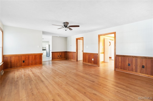 unfurnished living room with ceiling fan, light wood-type flooring, a textured ceiling, and wainscoting