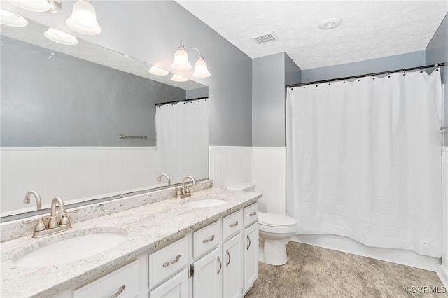 bathroom with wainscoting, a sink, visible vents, and a textured ceiling