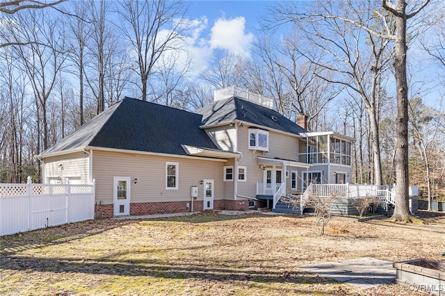 back of property with a sunroom, a chimney, roof with shingles, fence, and a wooden deck