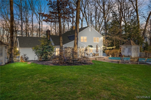 back of property featuring a patio area, a covered pool, a chimney, and a yard