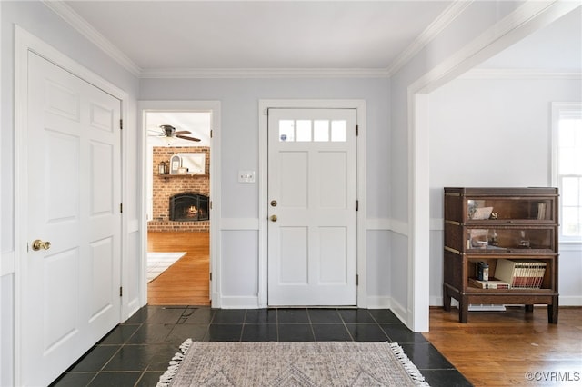 foyer featuring dark tile patterned floors, a brick fireplace, a ceiling fan, and crown molding