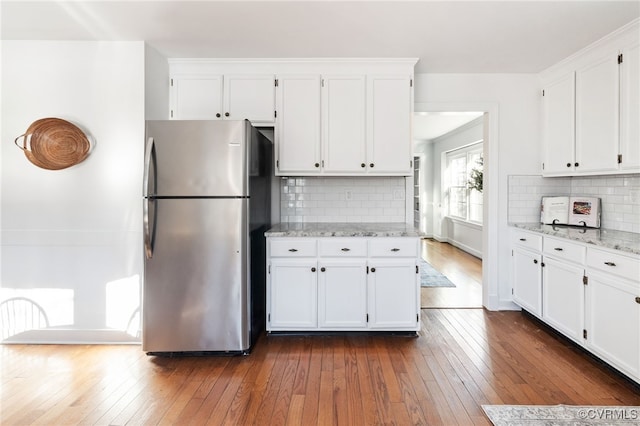 kitchen featuring decorative backsplash, white cabinets, dark wood finished floors, freestanding refrigerator, and light stone countertops