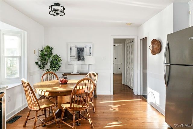 dining area featuring light wood-type flooring, visible vents, and wainscoting