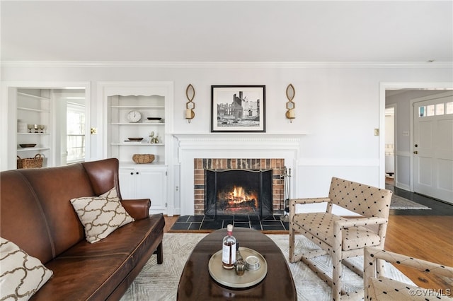 living area featuring built in shelves, a brick fireplace, wood finished floors, and crown molding