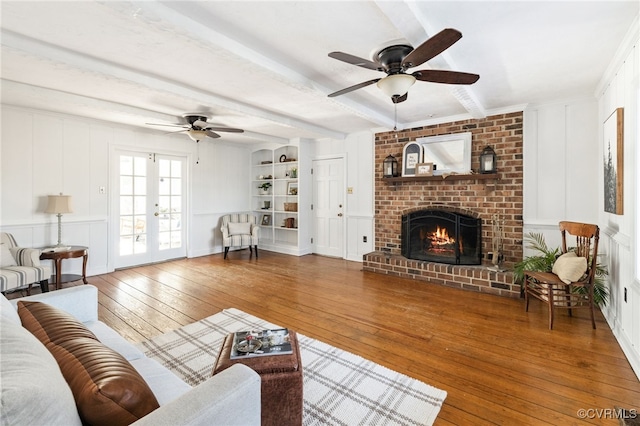 living room with built in features, french doors, wood-type flooring, a decorative wall, and beamed ceiling