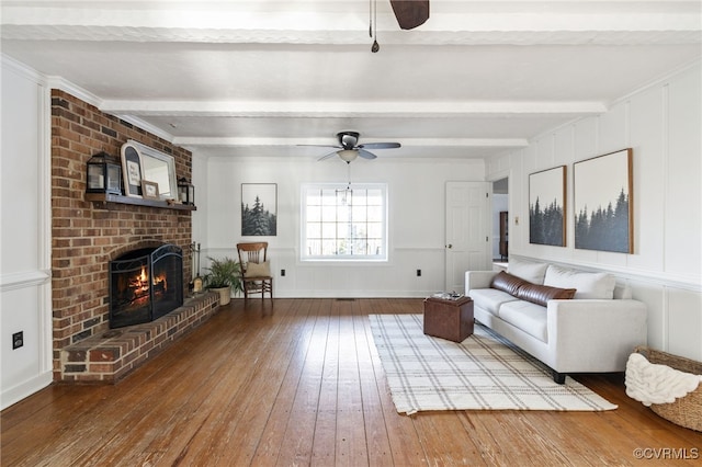 living area with wood-type flooring, a fireplace, beamed ceiling, and ceiling fan