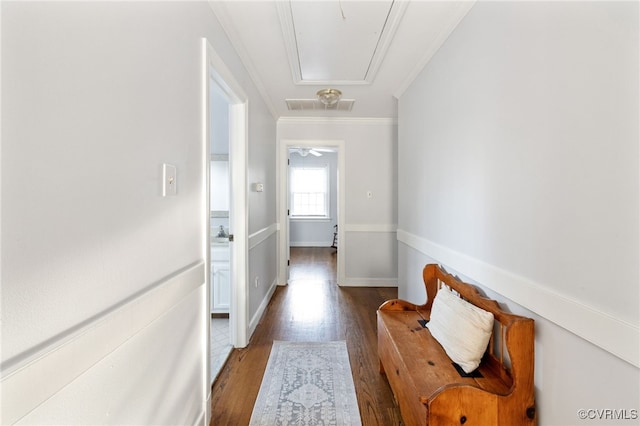 corridor with visible vents, attic access, dark wood-type flooring, ornamental molding, and baseboards