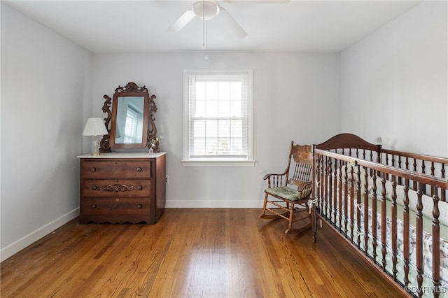 bedroom featuring a nursery area, ceiling fan, baseboards, and wood finished floors