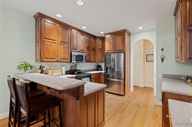 kitchen with sink, appliances with stainless steel finishes, a kitchen breakfast bar, light hardwood / wood-style floors, and kitchen peninsula