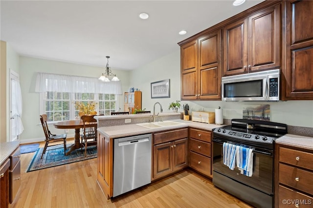 kitchen featuring appliances with stainless steel finishes, pendant lighting, sink, kitchen peninsula, and light hardwood / wood-style flooring