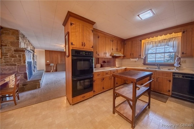 kitchen with brown cabinets, light countertops, a stone fireplace, black appliances, and a sink