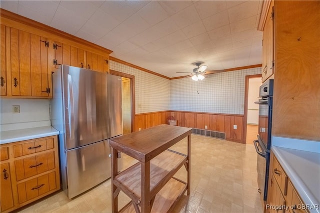 kitchen featuring a wainscoted wall, light countertops, freestanding refrigerator, brown cabinetry, and wallpapered walls