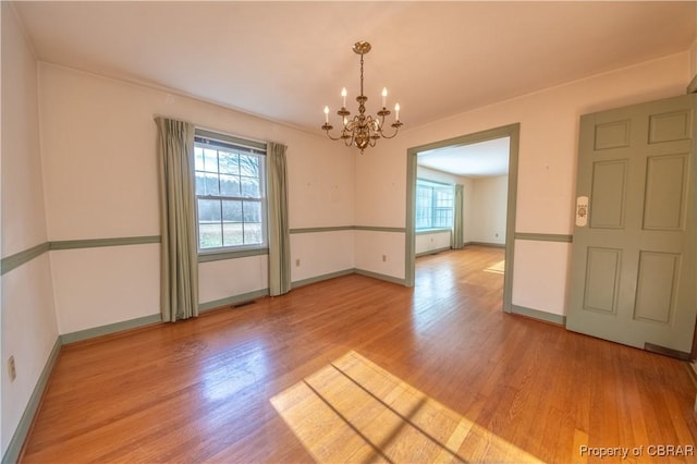 unfurnished room featuring baseboards, wood finished floors, visible vents, and a notable chandelier