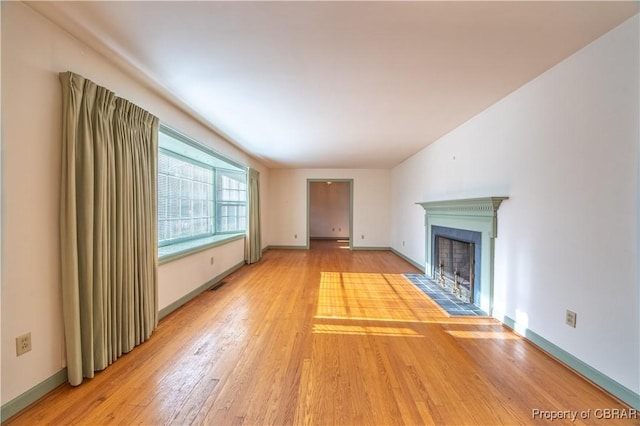 unfurnished living room with a fireplace with flush hearth, visible vents, baseboards, and wood finished floors