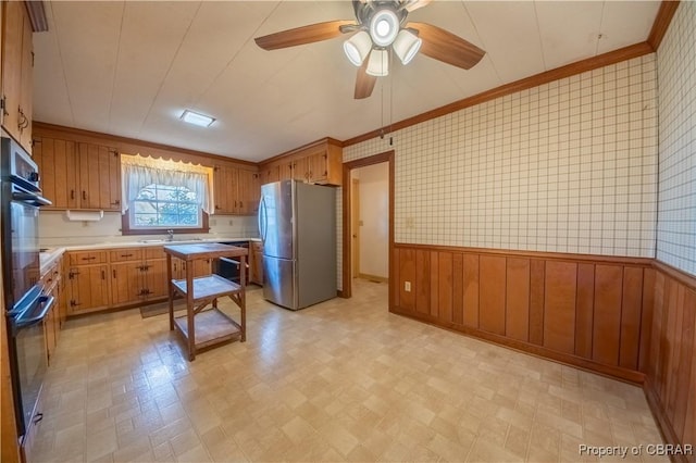 kitchen featuring brown cabinetry, a wainscoted wall, freestanding refrigerator, light countertops, and a sink