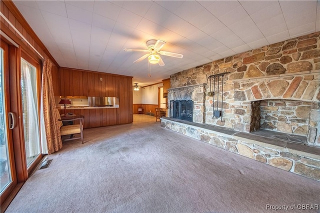 unfurnished living room with carpet floors, a fireplace, visible vents, wood walls, and ceiling fan