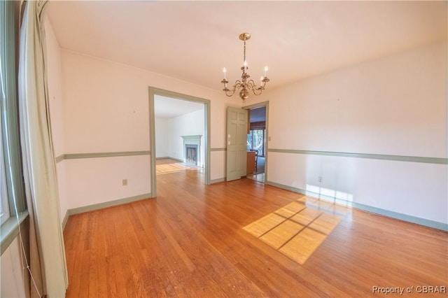 spare room with baseboards, a fireplace, a chandelier, and wood finished floors