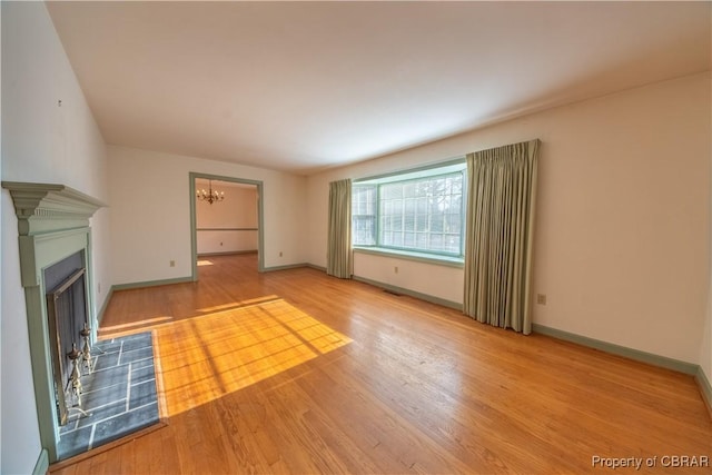 unfurnished living room with baseboards, a fireplace, wood finished floors, and a notable chandelier