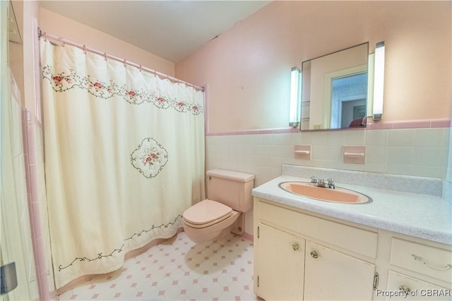 bathroom featuring toilet, a wainscoted wall, tile patterned floors, vanity, and tile walls